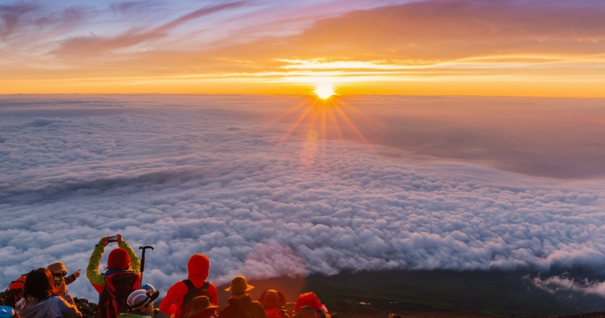 Climbers watching the sunrise above a sea of clouds on Mt. Fuji