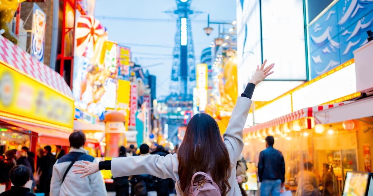 A traveler in Shinsekai with Tsutenkaku tower beyond