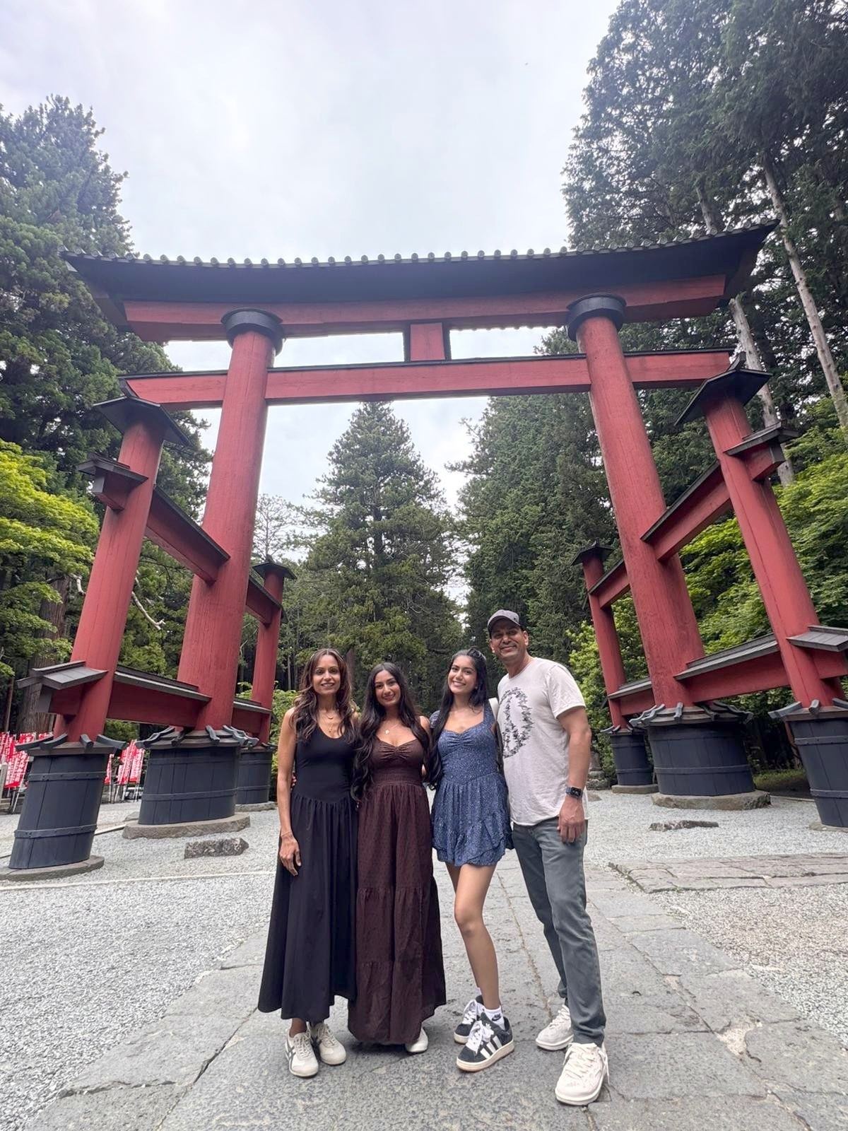 The family at a red torii gate in a cedar forest